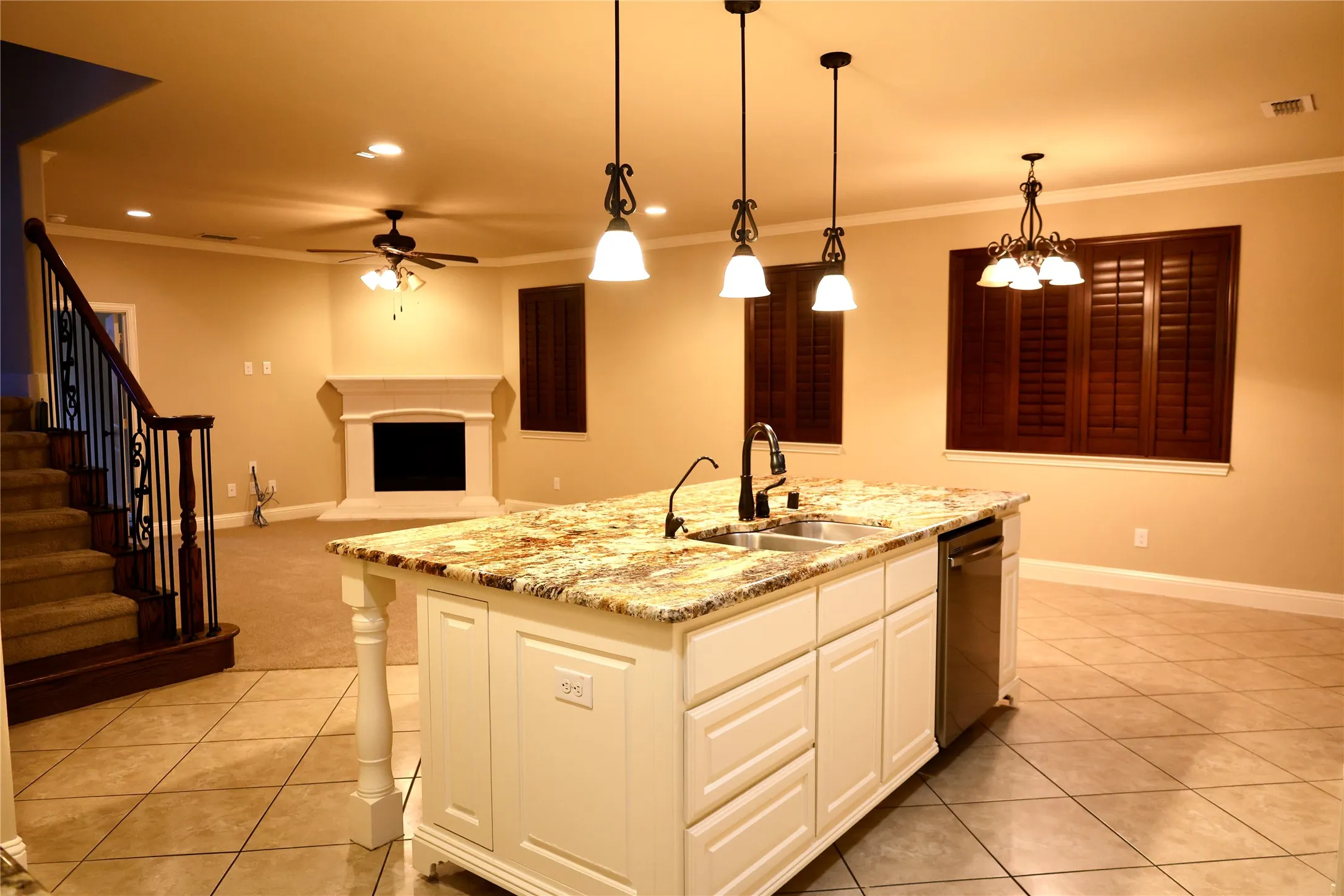 Kitchen with ornamental molding, light stone countertops, decorative light fixtures, a center island with sink, and white cabinetry