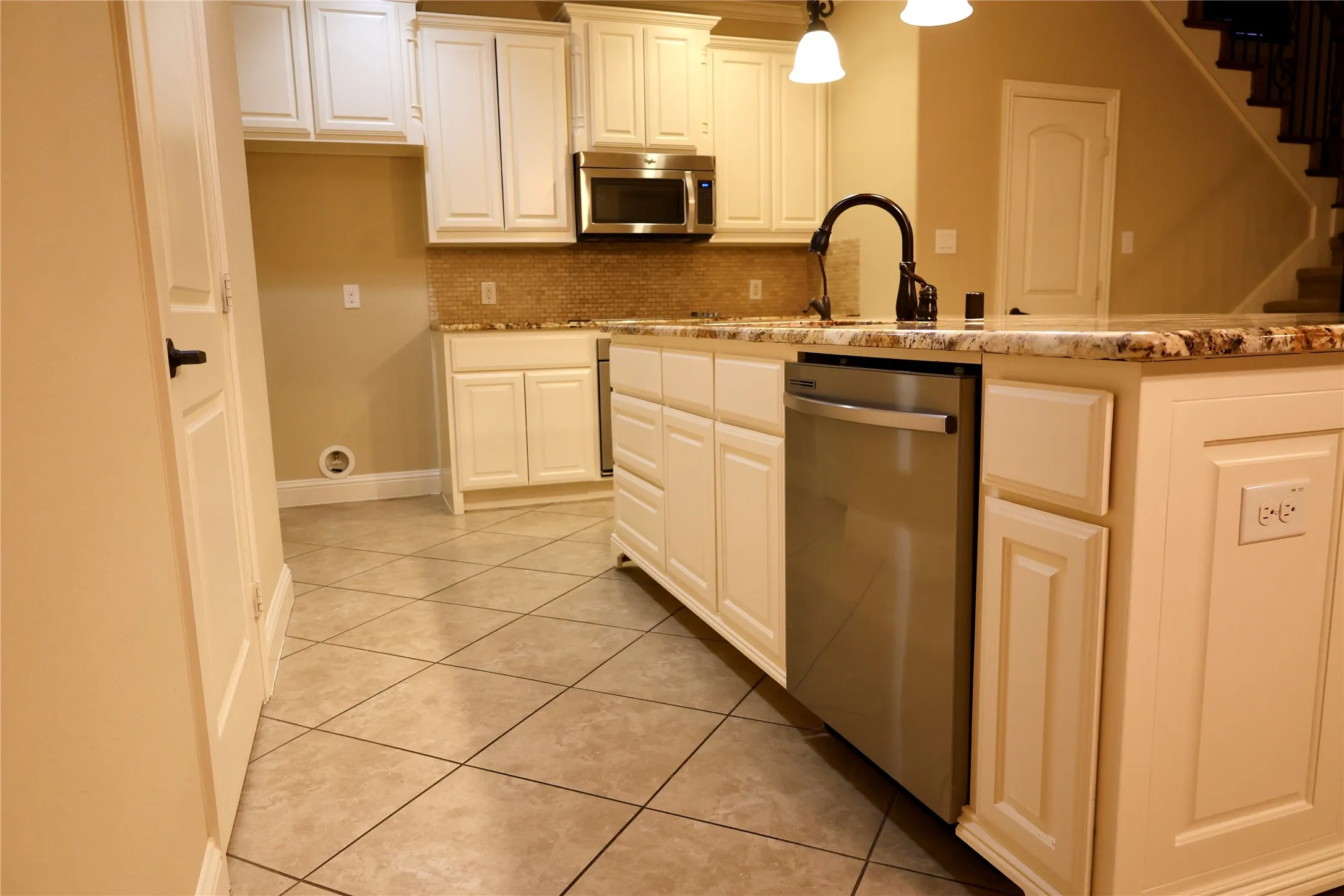 Kitchen with light stone countertops, stainless steel appliances, backsplash, and hanging light fixtures