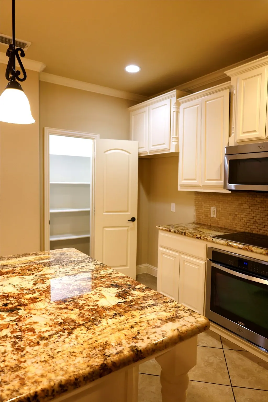 Kitchen with light stone counters, white cabinets, stainless steel appliances, ornamental molding, and light tile patterned floors