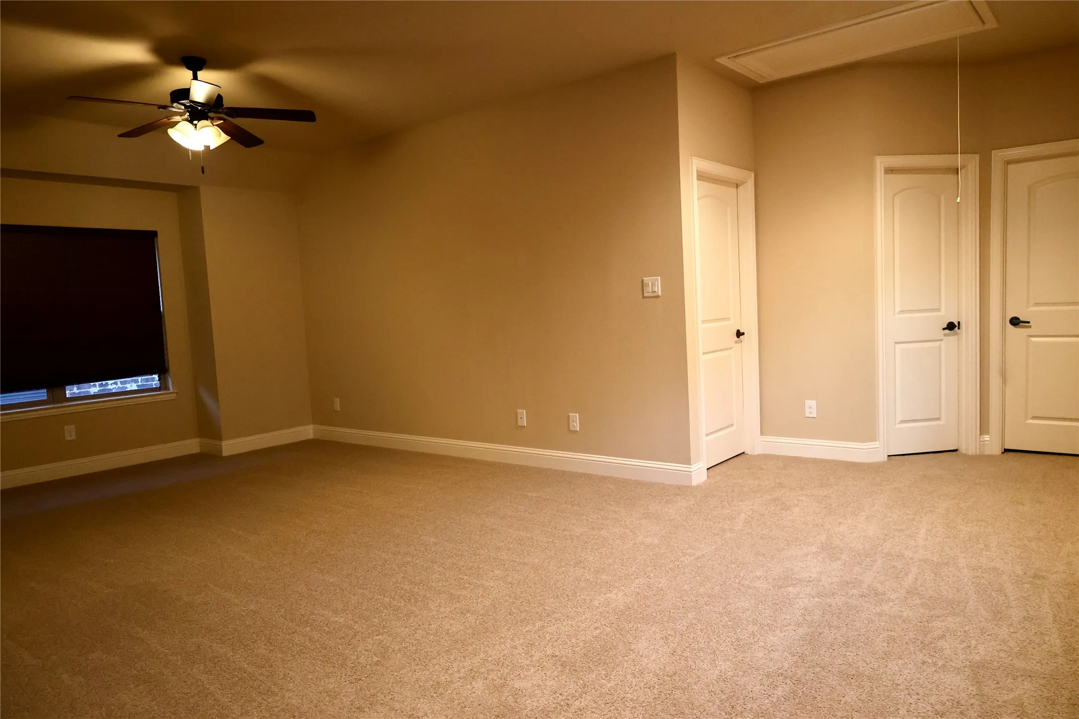 Empty room with attic access, light carpet, and a ceiling fan