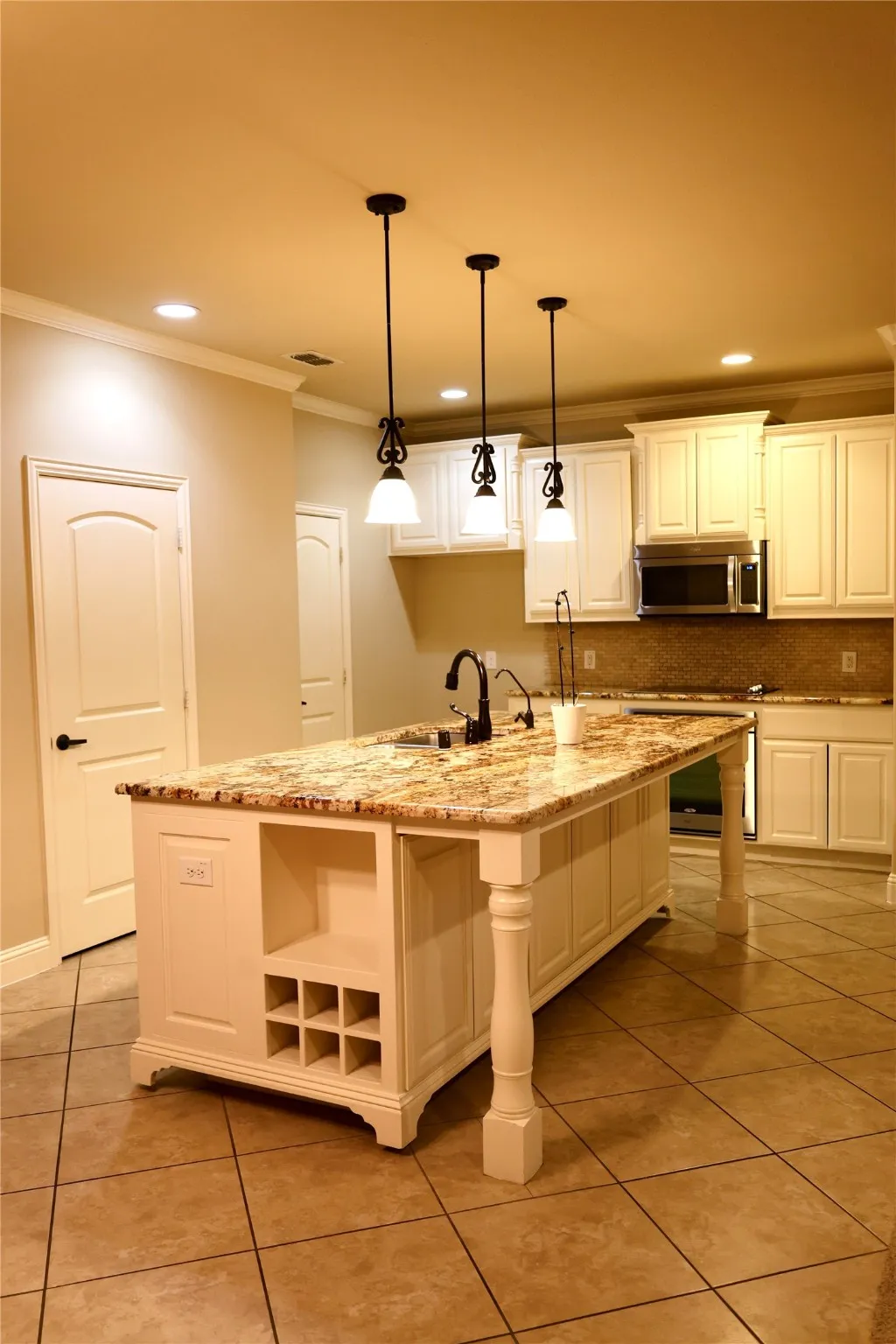 Kitchen with crown molding, light tile patterned floors, light stone counters, decorative backsplash, and a center island with sink
