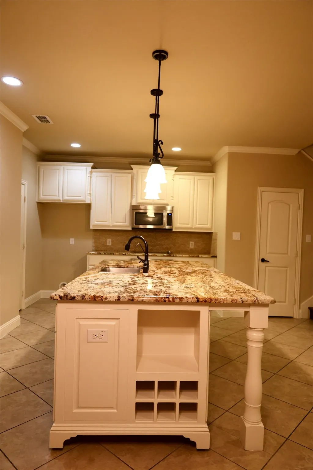 Kitchen with ornamental molding, light stone counters, white cabinets, hanging light fixtures, and tasteful backsplash