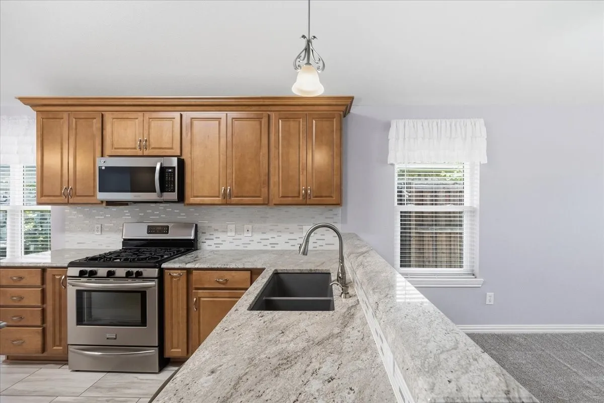 Kitchen featuring appliances with stainless steel finishes, brown cabinetry, tasteful backsplash, and light stone counters