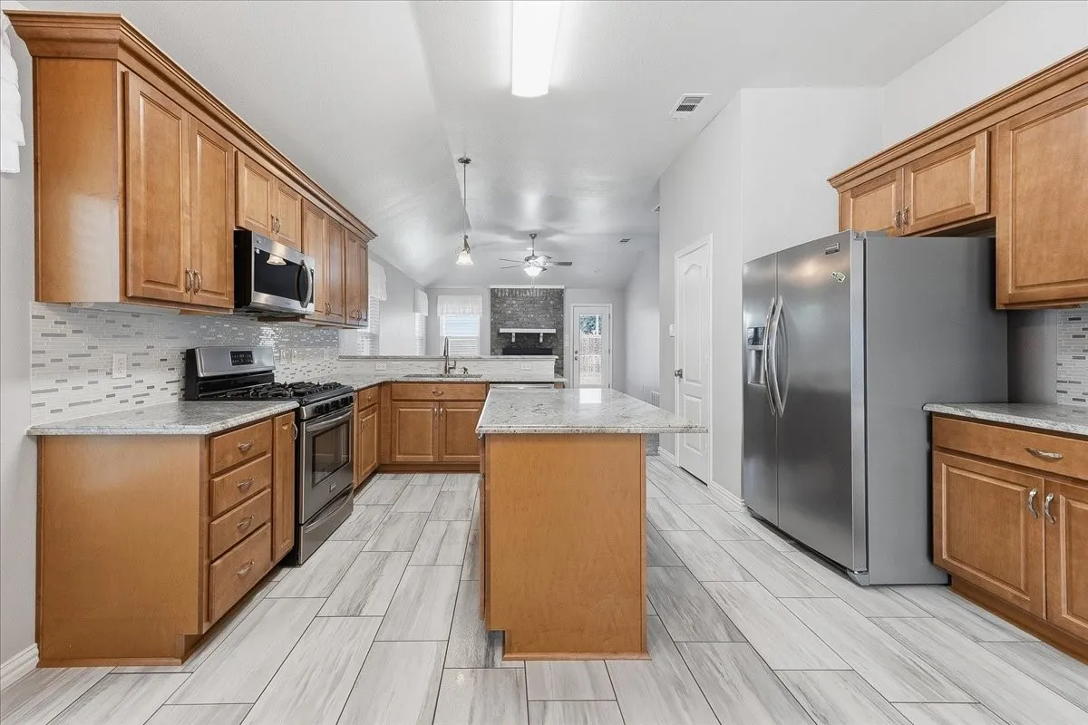Kitchen with backsplash, brown cabinets, appliances with stainless steel finishes, a kitchen island, and a ceiling fan