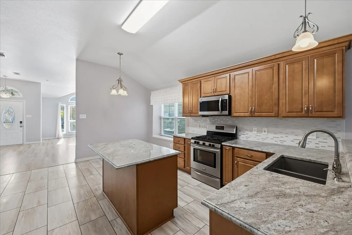 Kitchen featuring pendant lighting, a center island, stainless steel appliances, brown cabinets, and vaulted ceiling