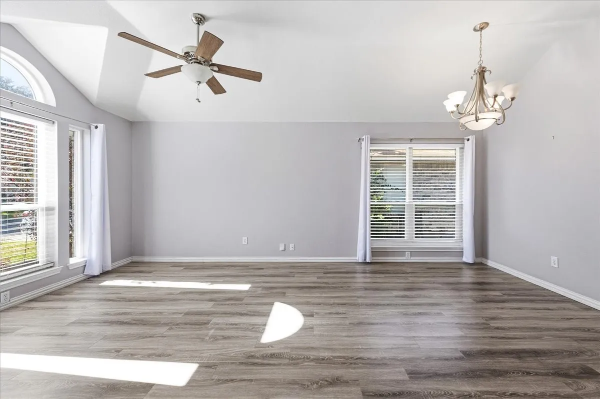 Empty room with vaulted ceiling, wood finished floors, a chandelier, and ceiling fan