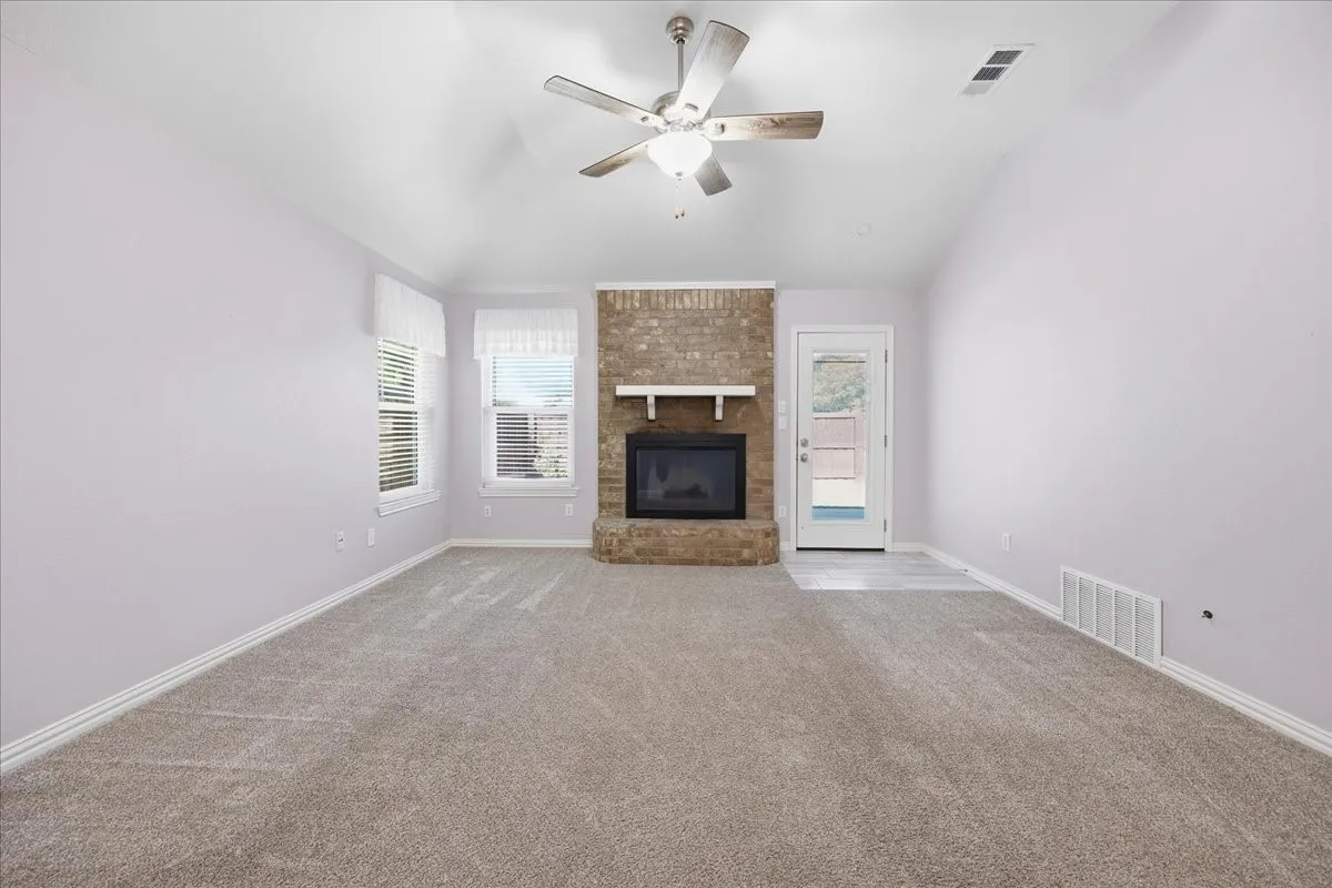 Unfurnished living room with plenty of natural light, lofted ceiling, ceiling fan, carpet flooring, and a brick fireplace