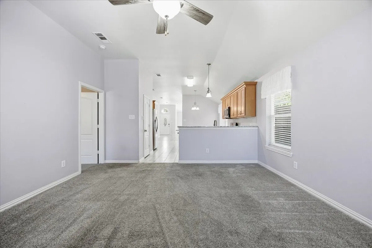 Unfurnished living room featuring vaulted ceiling, ceiling fan, and light colored carpet