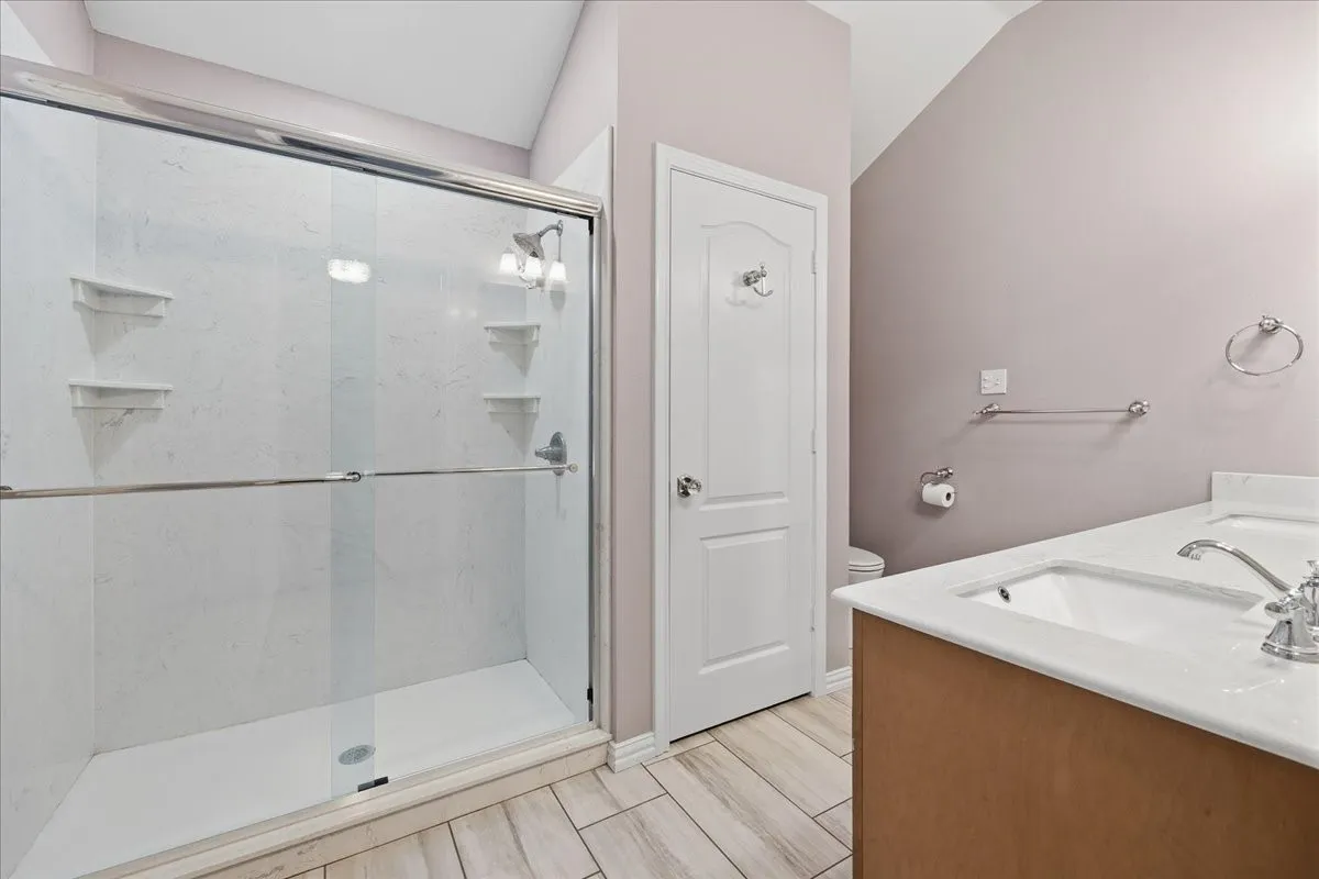 Bathroom featuring double vanity, a marble finish shower, and wood tiled floors