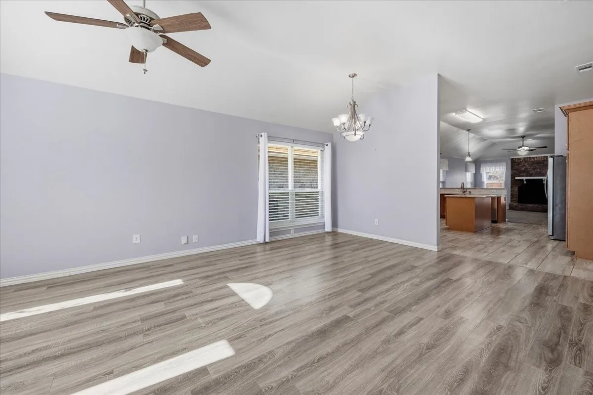Unfurnished living room featuring a ceiling fan, vaulted ceiling, light wood-style floors, and a chandelier