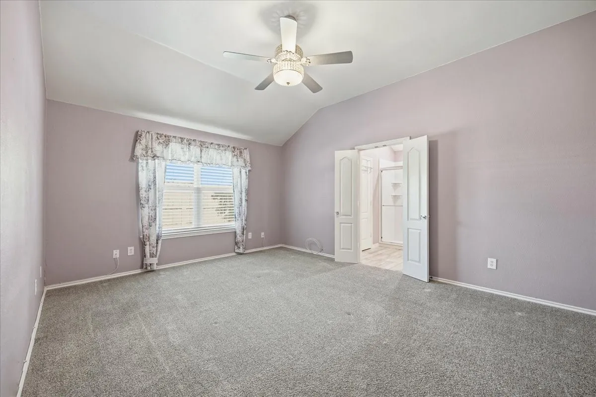 Unfurnished bedroom with a ceiling fan, carpet flooring, and vaulted ceiling