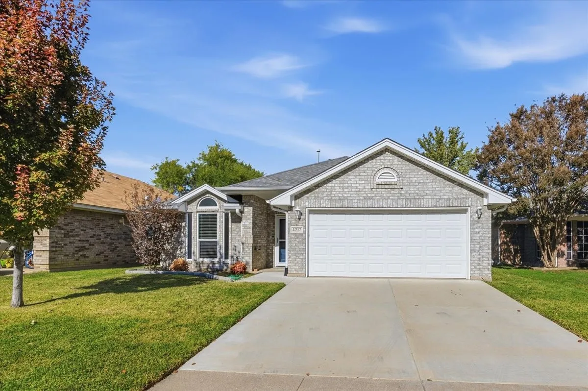 Ranch-style home with a front lawn, driveway, an attached garage, and brick siding