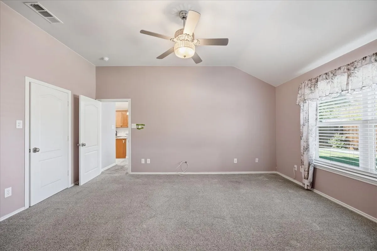 Unfurnished bedroom featuring vaulted ceiling, light carpet, and ceiling fan