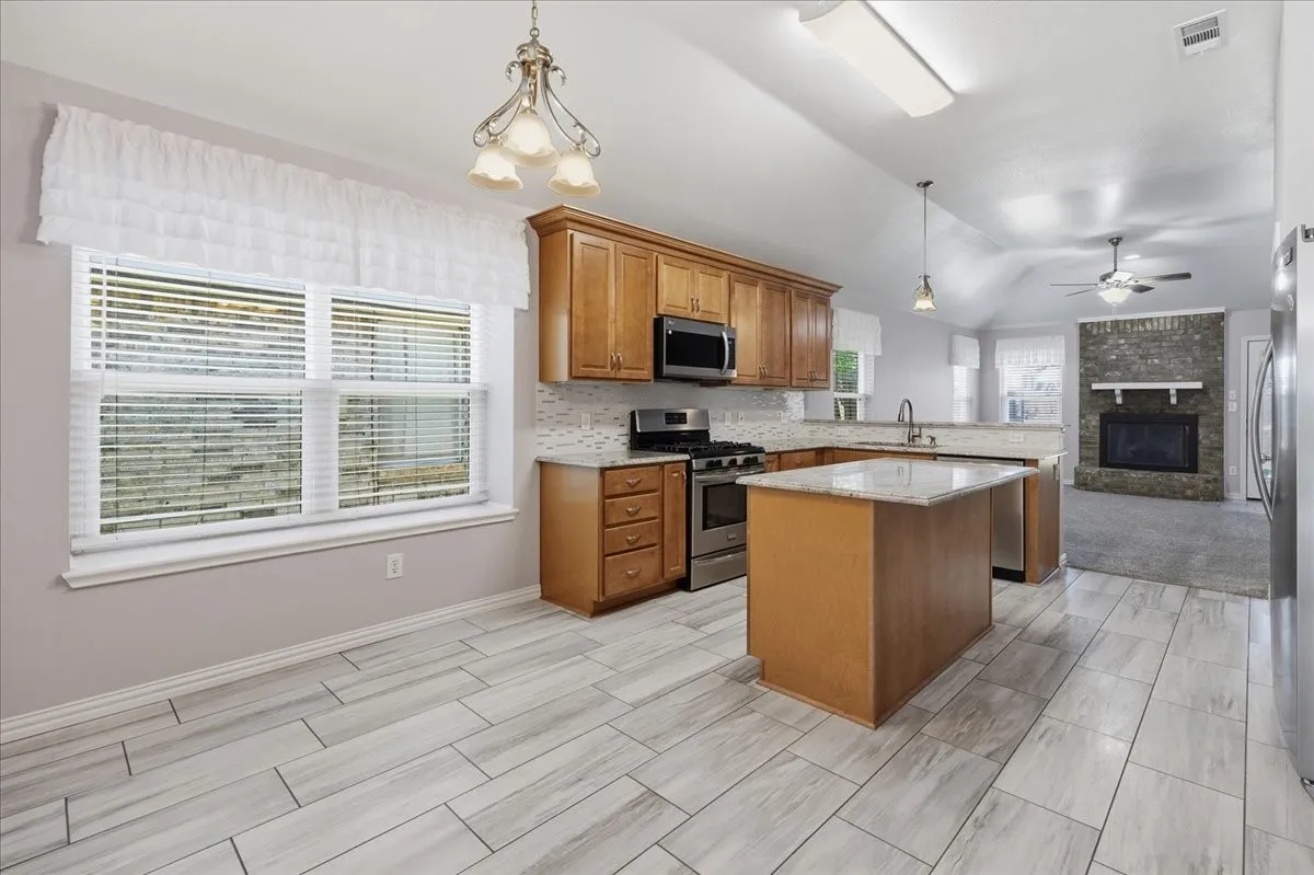 Kitchen featuring stainless steel appliances, decorative light fixtures, brown cabinets, open floor plan, and a kitchen island