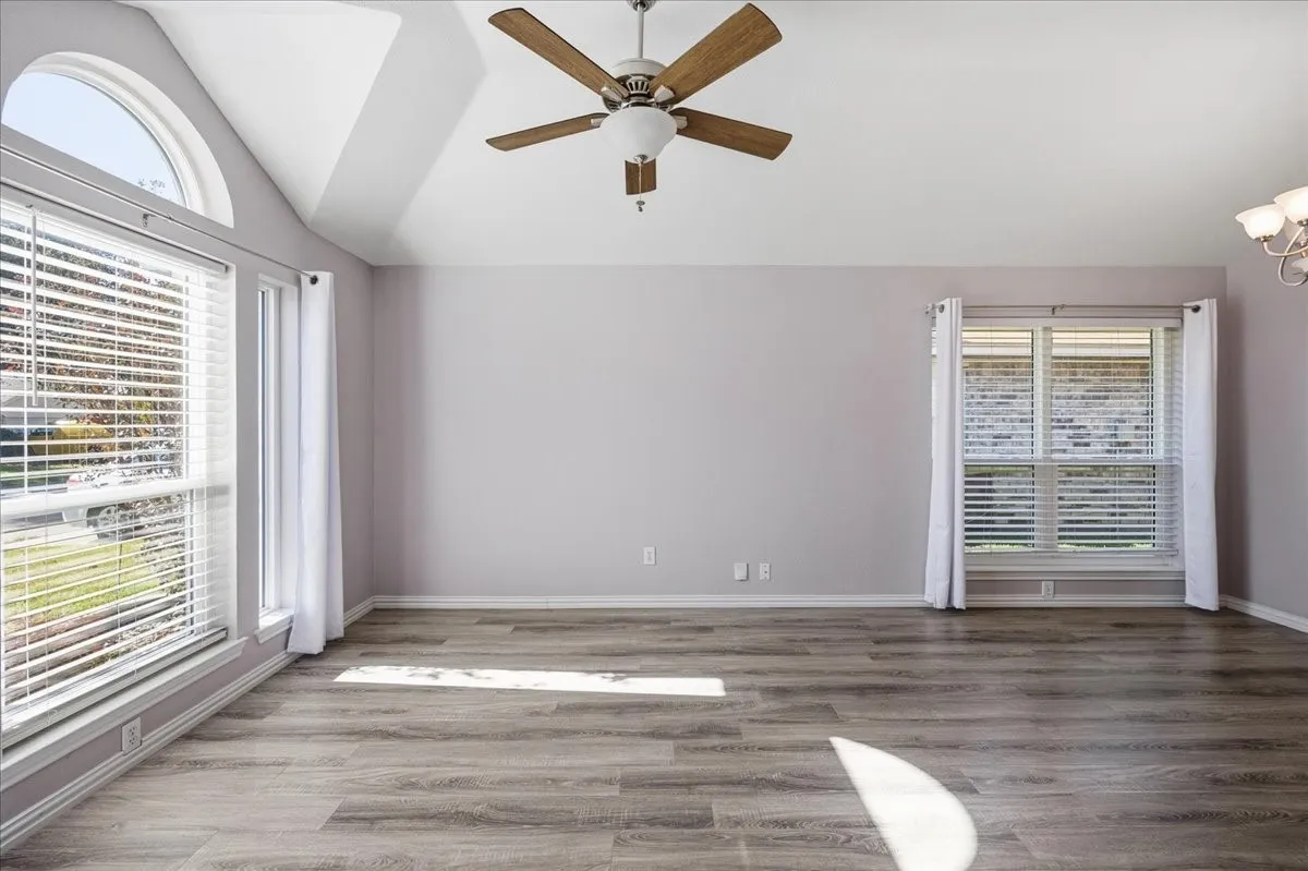 Empty room featuring vaulted ceiling, wood finished floors, a chandelier, and ceiling fan