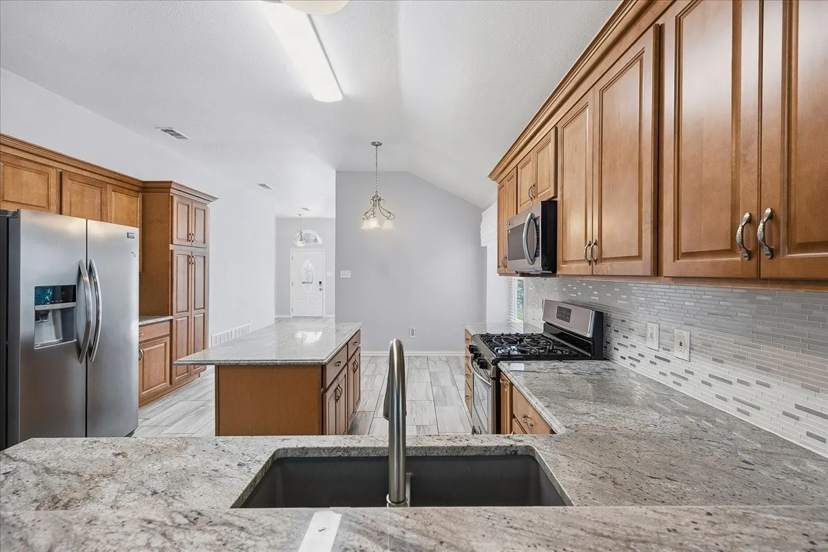 Kitchen featuring brown cabinetry, a kitchen island, stainless steel appliances, vaulted ceiling, and pendant lighting