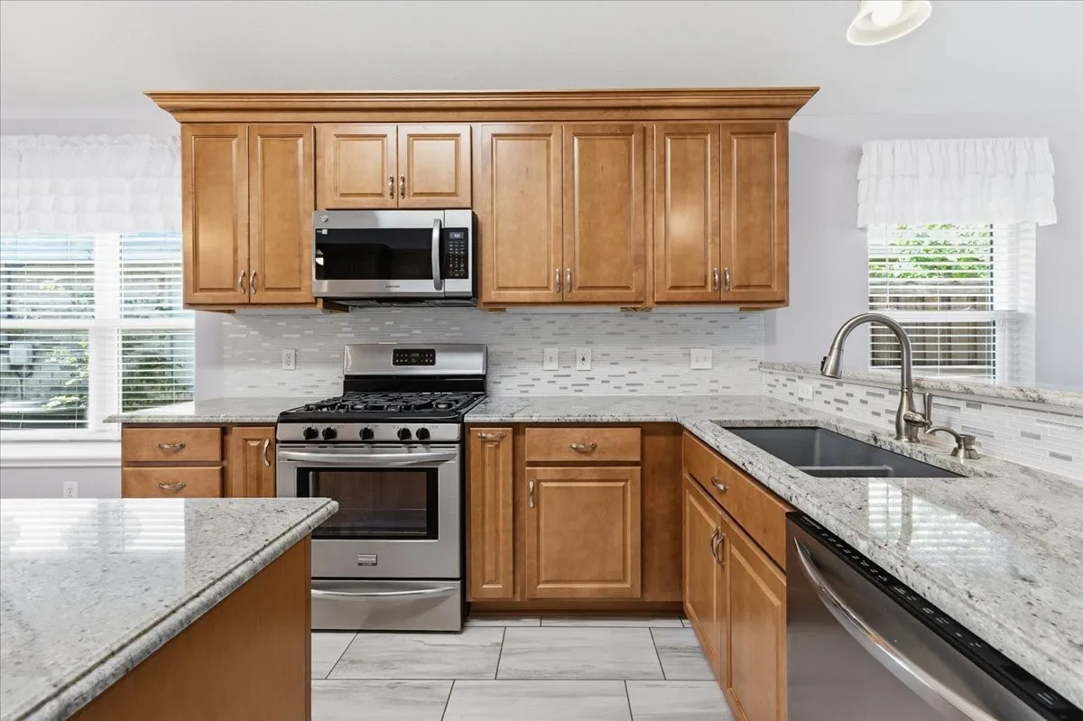 Kitchen with brown cabinets, light stone counters, appliances with stainless steel finishes, and backsplash
