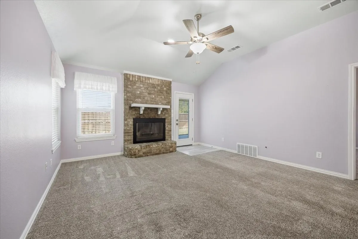 Unfurnished living room with vaulted ceiling, carpet floors, a brick fireplace, and a ceiling fan
