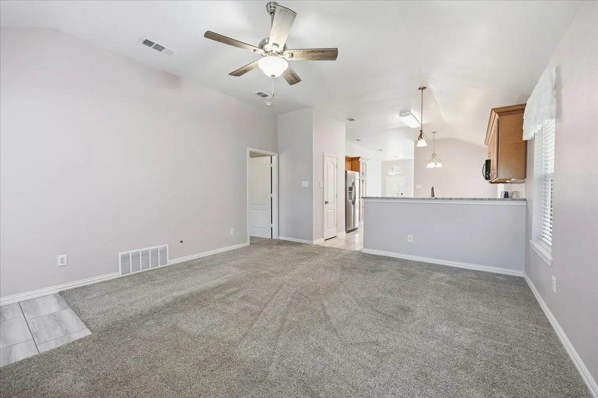 Unfurnished living room featuring lofted ceiling, light colored carpet, and ceiling fan