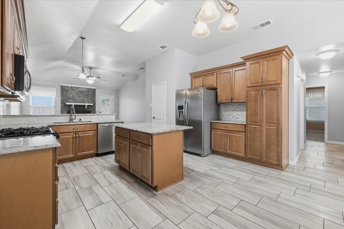 Kitchen featuring tasteful backsplash, brown cabinets, light stone counters, appliances with stainless steel finishes, and a peninsula
