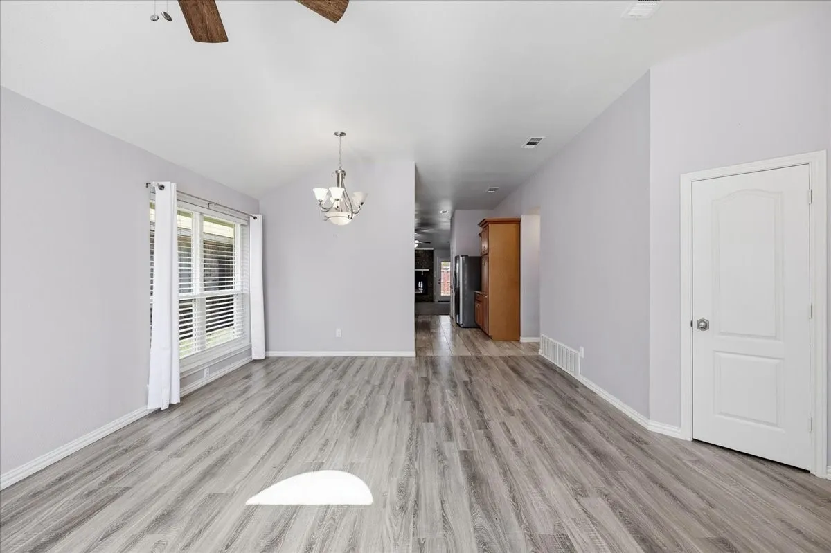 Unfurnished living room featuring ceiling fan, light wood-type flooring, a chandelier, and vaulted ceiling