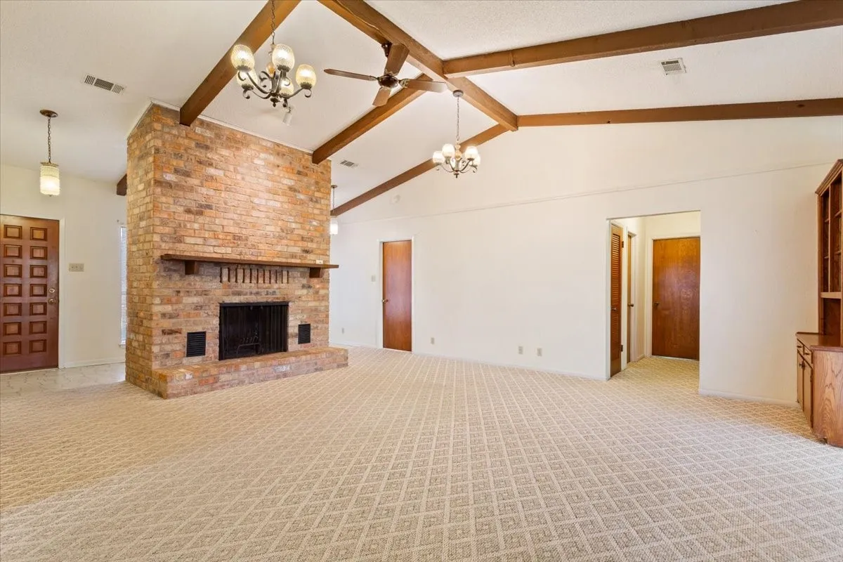 Unfurnished living room featuring beamed ceiling, a chandelier, a fireplace, light carpet, and a ceiling fan