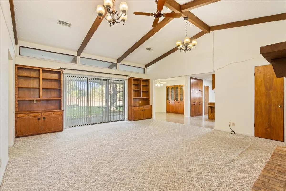 Unfurnished living room featuring high vaulted ceiling, beam ceiling, light carpet, a chandelier, and a ceiling fan