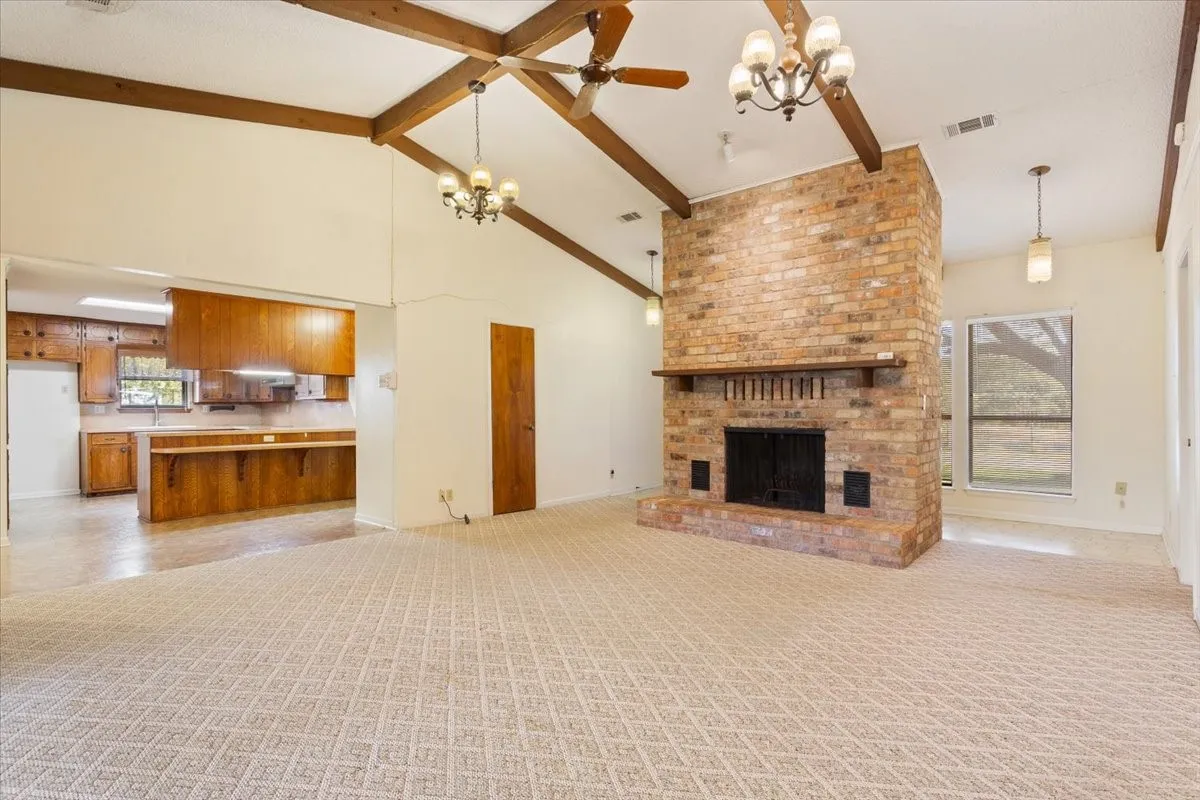 Unfurnished living room with high vaulted ceiling, beamed ceiling, a chandelier, a brick fireplace, and light carpet