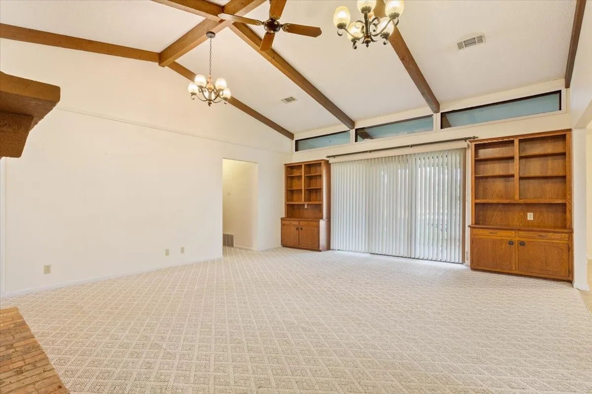 Unfurnished living room featuring a chandelier, beam ceiling, high vaulted ceiling, and light carpet