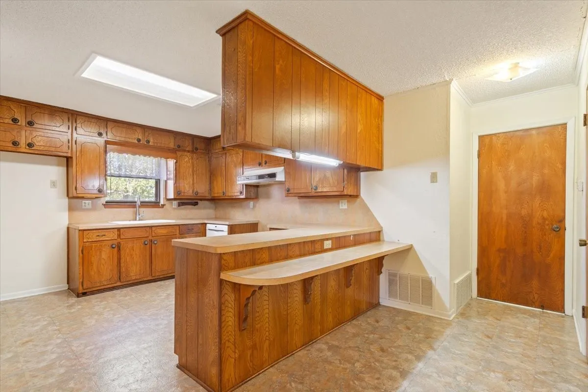 Kitchen featuring brown cabinetry, light countertops, a breakfast bar, a peninsula, and ornamental molding
