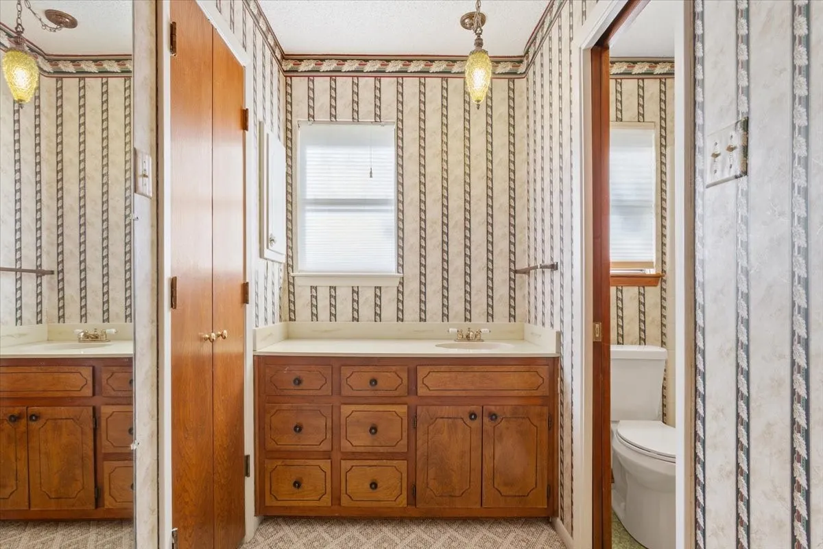 Full bath with two vanities, plenty of natural light, and wallpapered walls