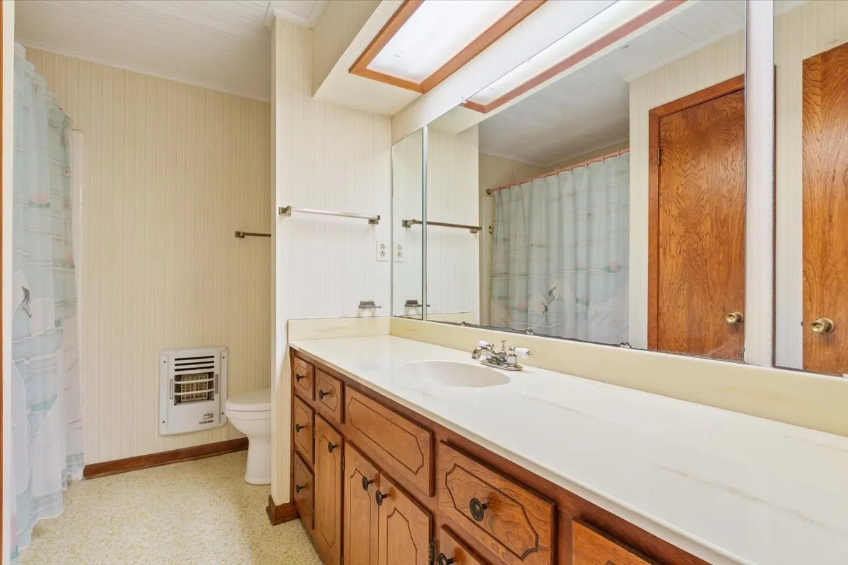 Full bath with curtained shower, heating unit, and vanity