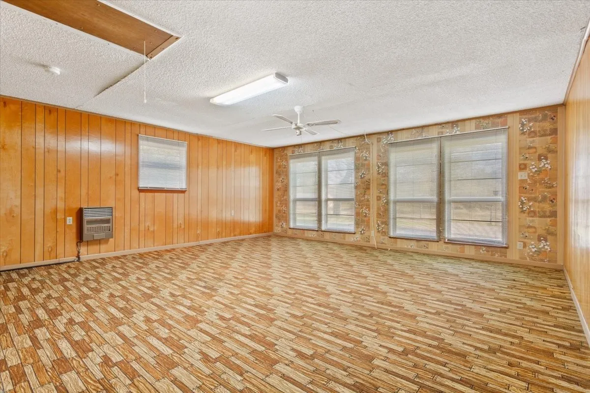 Empty room featuring plenty of natural light, wooden walls, attic access, heating unit, and a ceiling fan