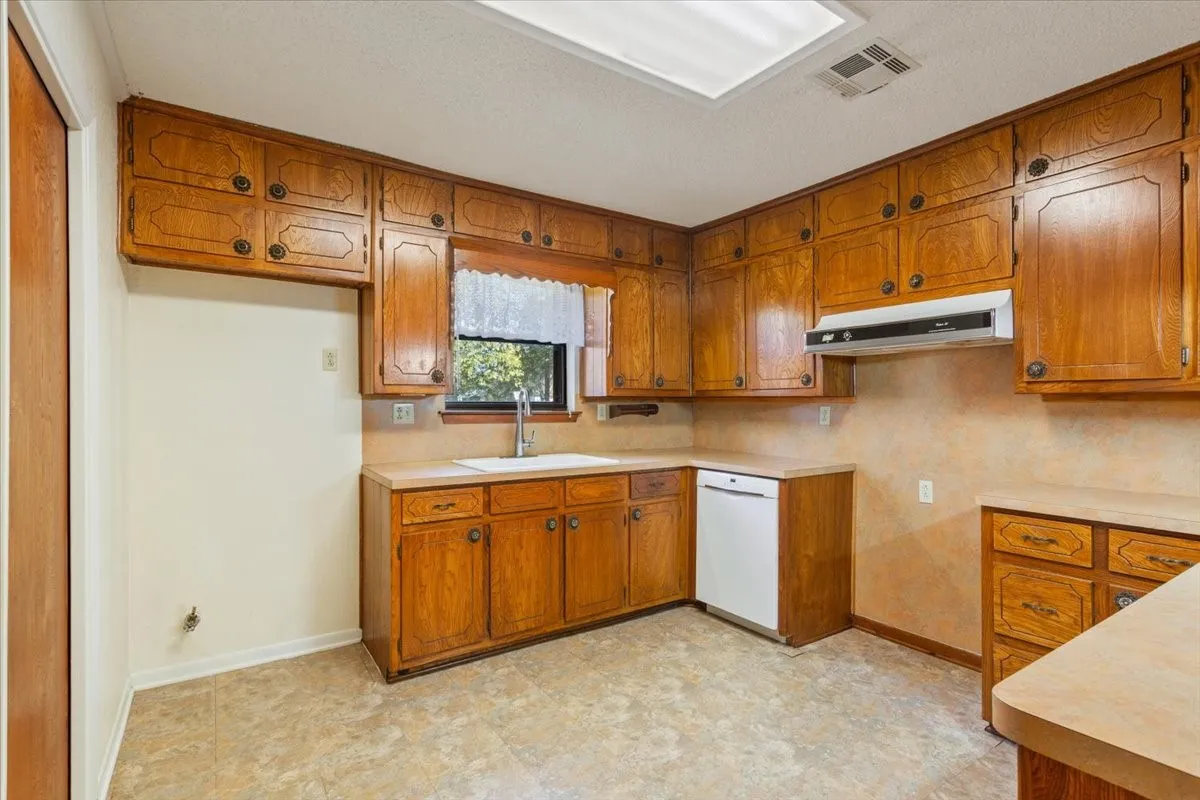 Kitchen with brown cabinetry, light countertops, dishwasher, and under cabinet range hood