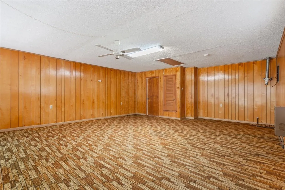 Spare room featuring wood walls, ceiling fan, light wood-style flooring, and a textured ceiling