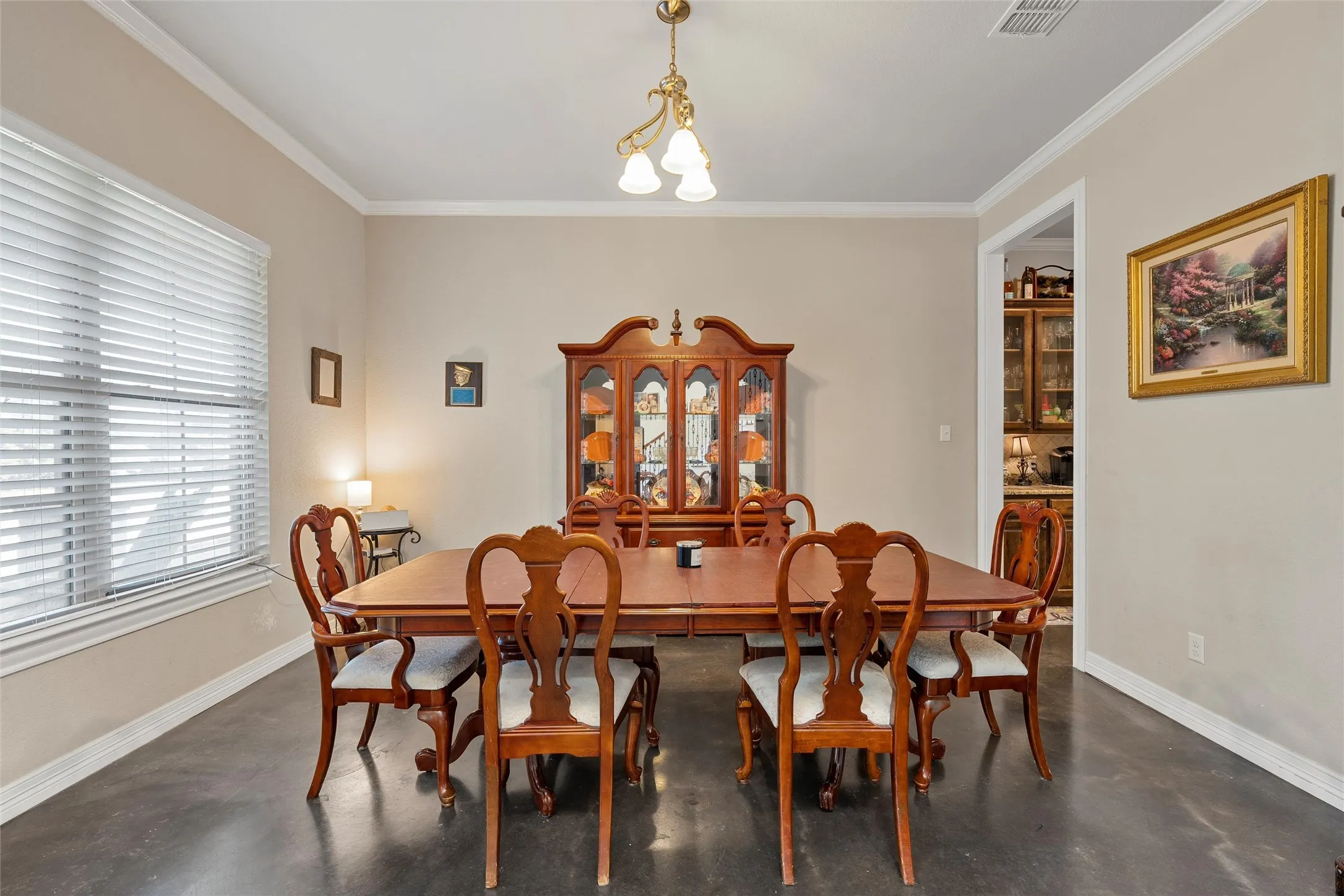 Dining room featuring finished concrete flooring, ornamental molding, and a chandelier