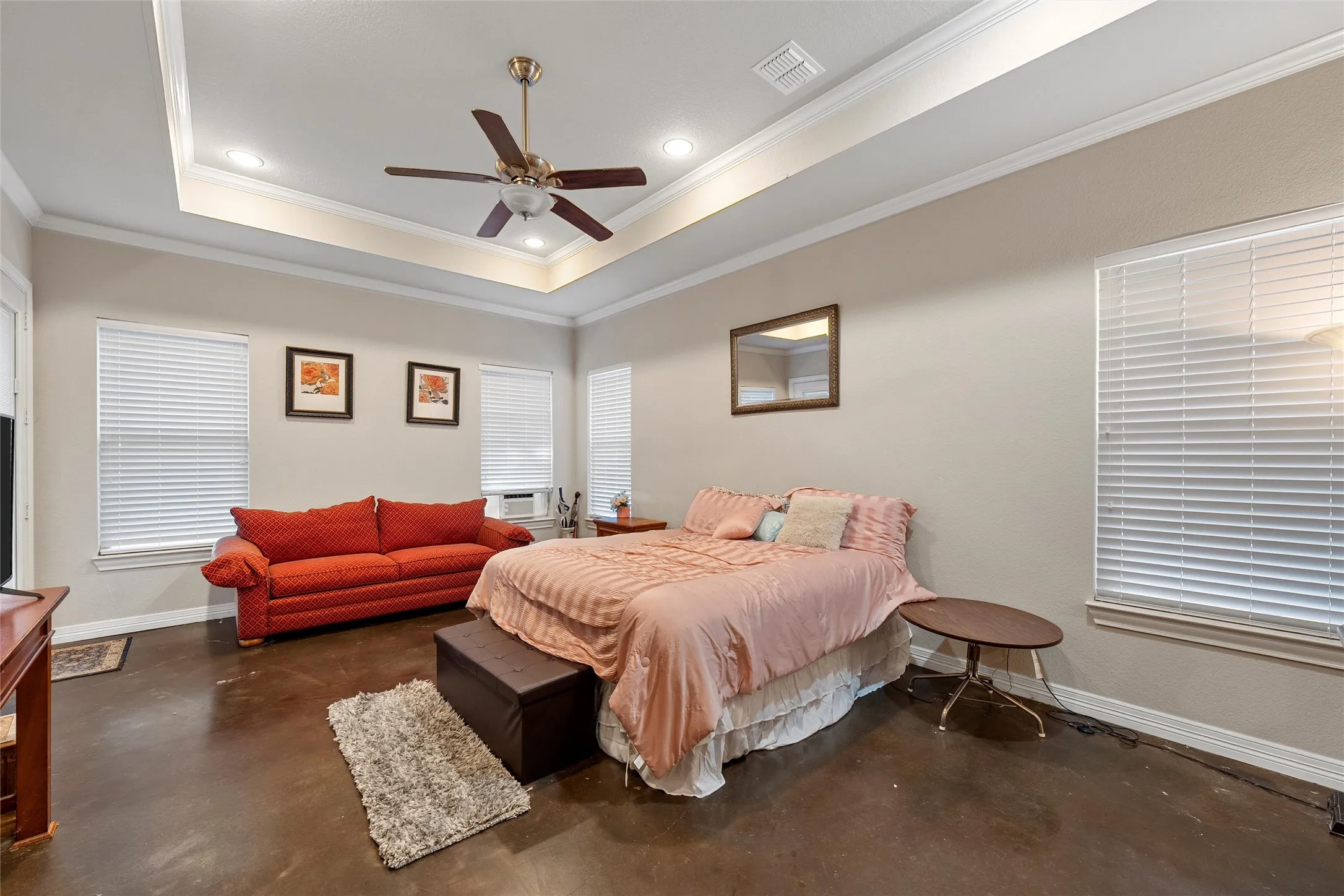 Bedroom with a tray ceiling, finished concrete flooring, crown molding, a ceiling fan, and recessed lighting