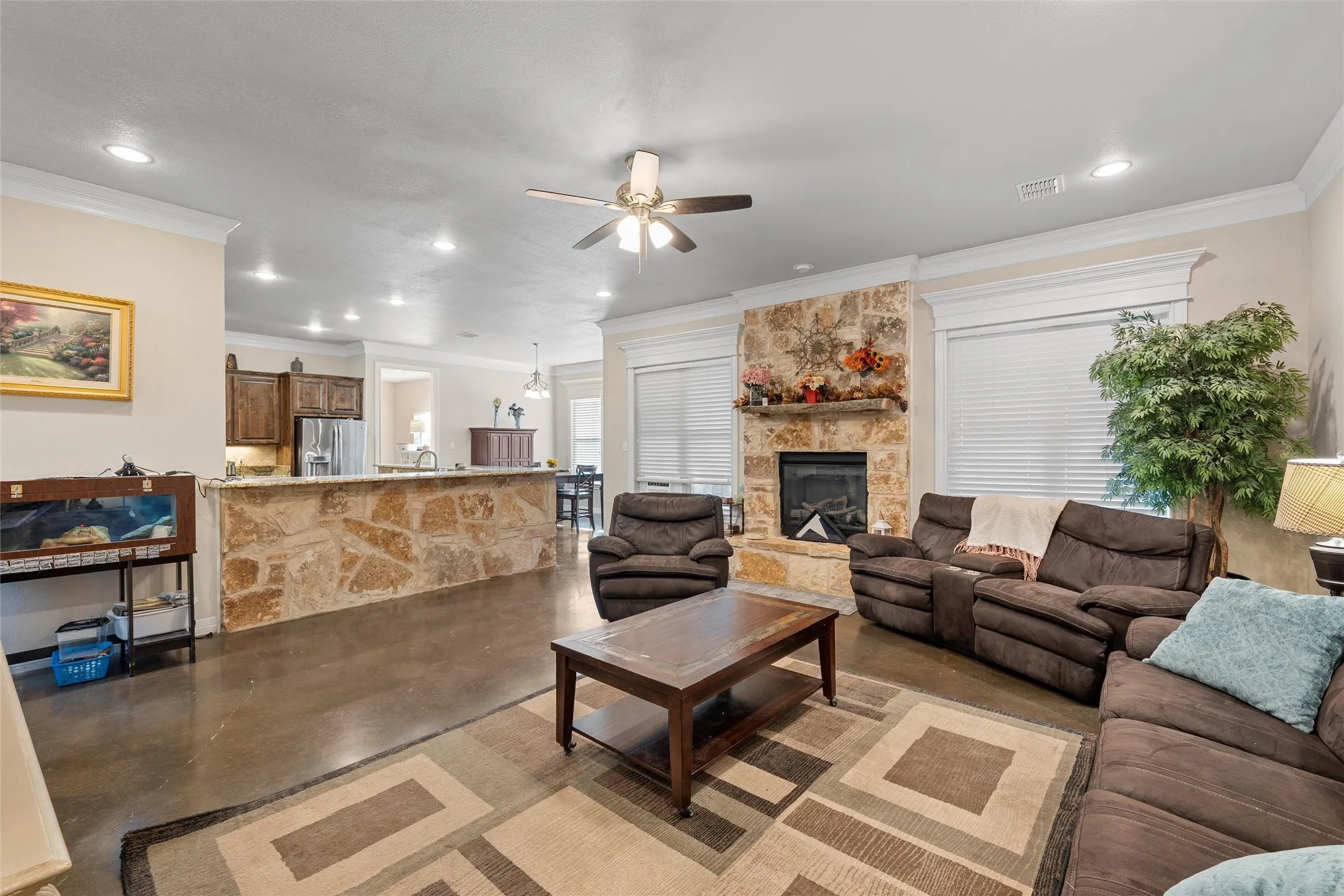 Living area featuring finished concrete floors, ornamental molding, a ceiling fan, a fireplace, and recessed lighting