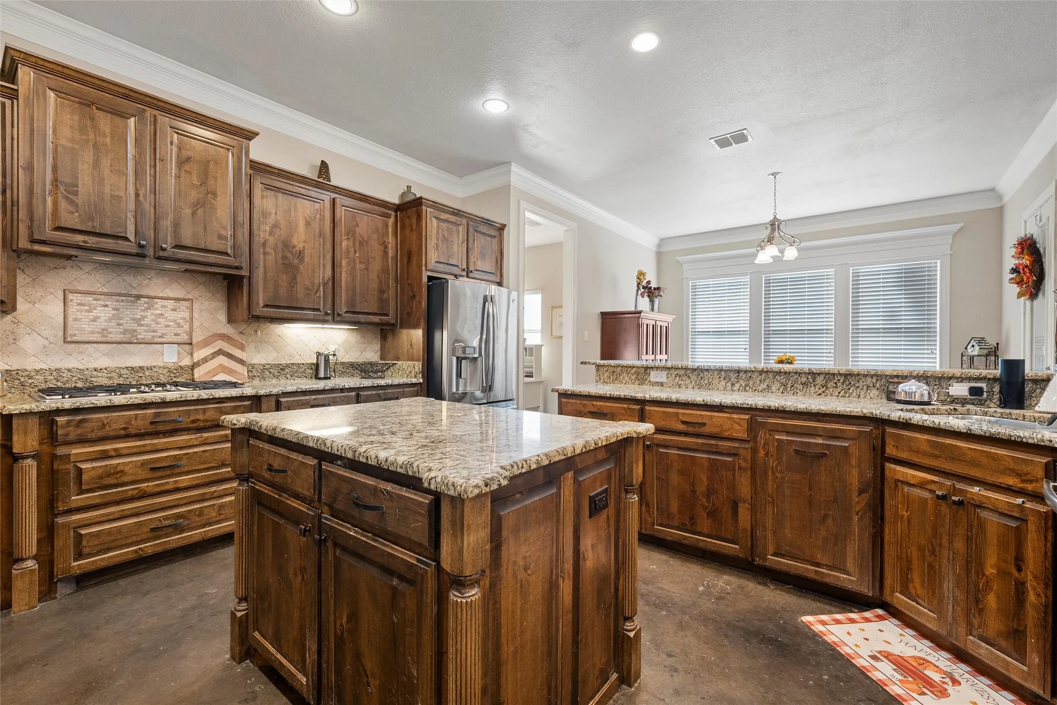 Kitchen featuring backsplash, crown molding, concrete flooring, decorative light fixtures, and a center island
