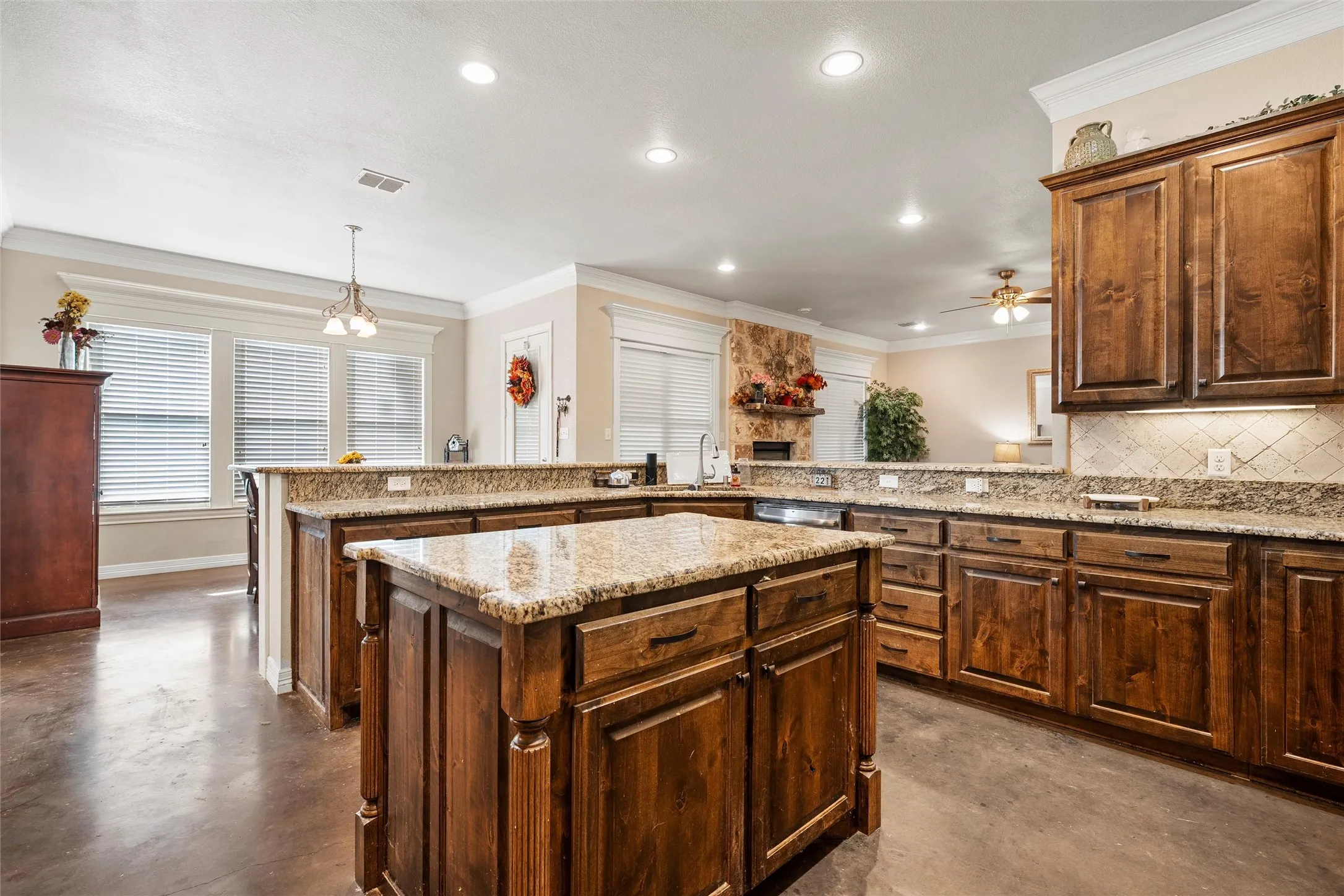 Kitchen featuring finished concrete flooring, ornamental molding, pendant lighting, a center island, and light stone counters