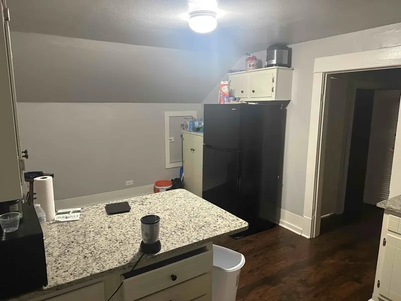 Kitchen with a peninsula, lofted ceiling, black appliances, light stone counters, and white cabinetry