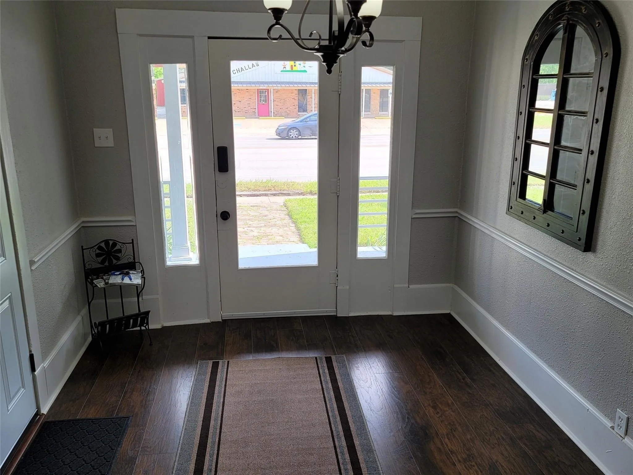 Foyer entrance with an inviting chandelier, a textured wall, dark wood-style floors, and baseboards