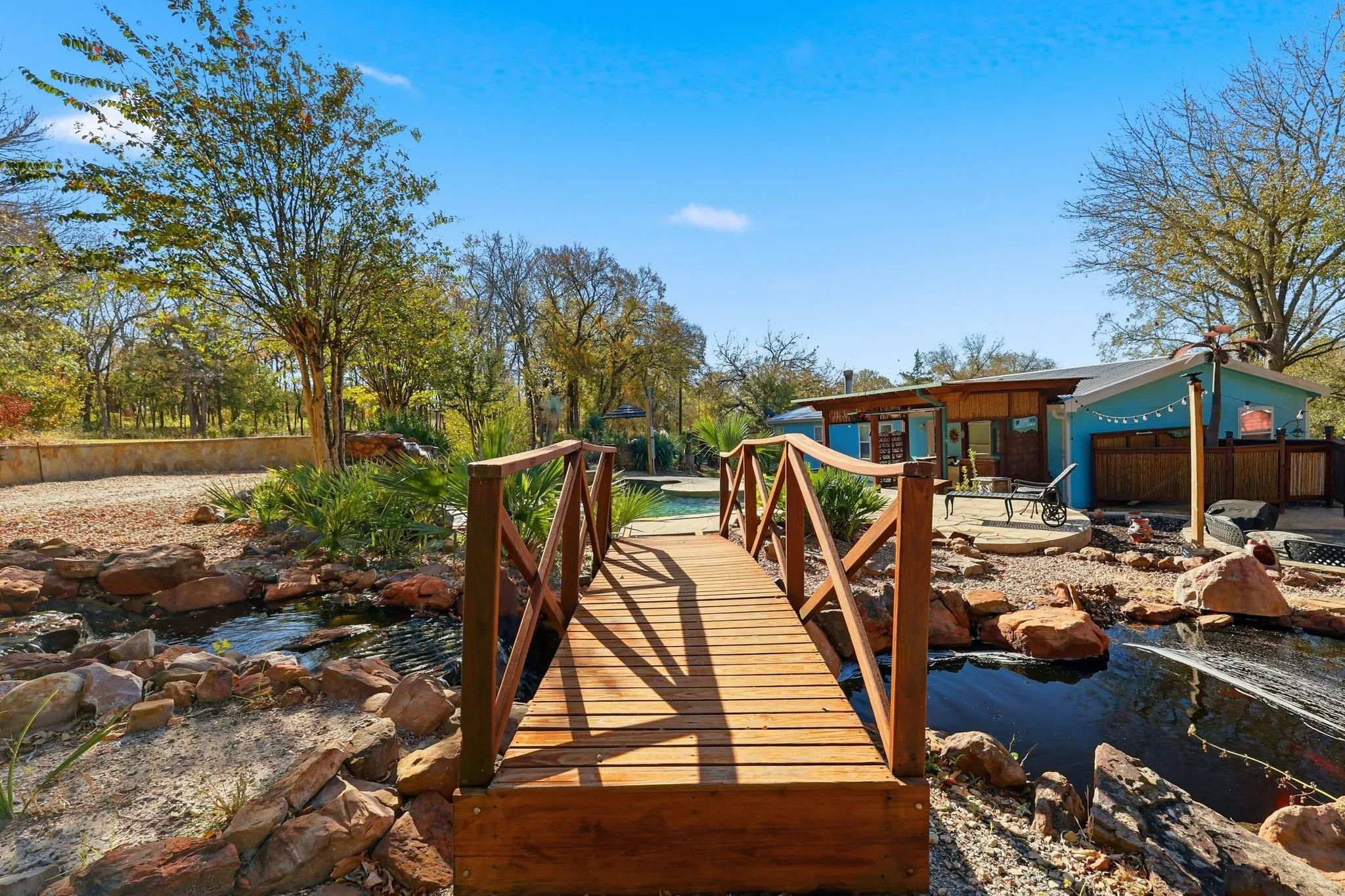Wooden Footbridge Arching Over the Koi Pond with a Gentle Waterfall Cascading Nearby. A Serene Walkway Through the Landscape.