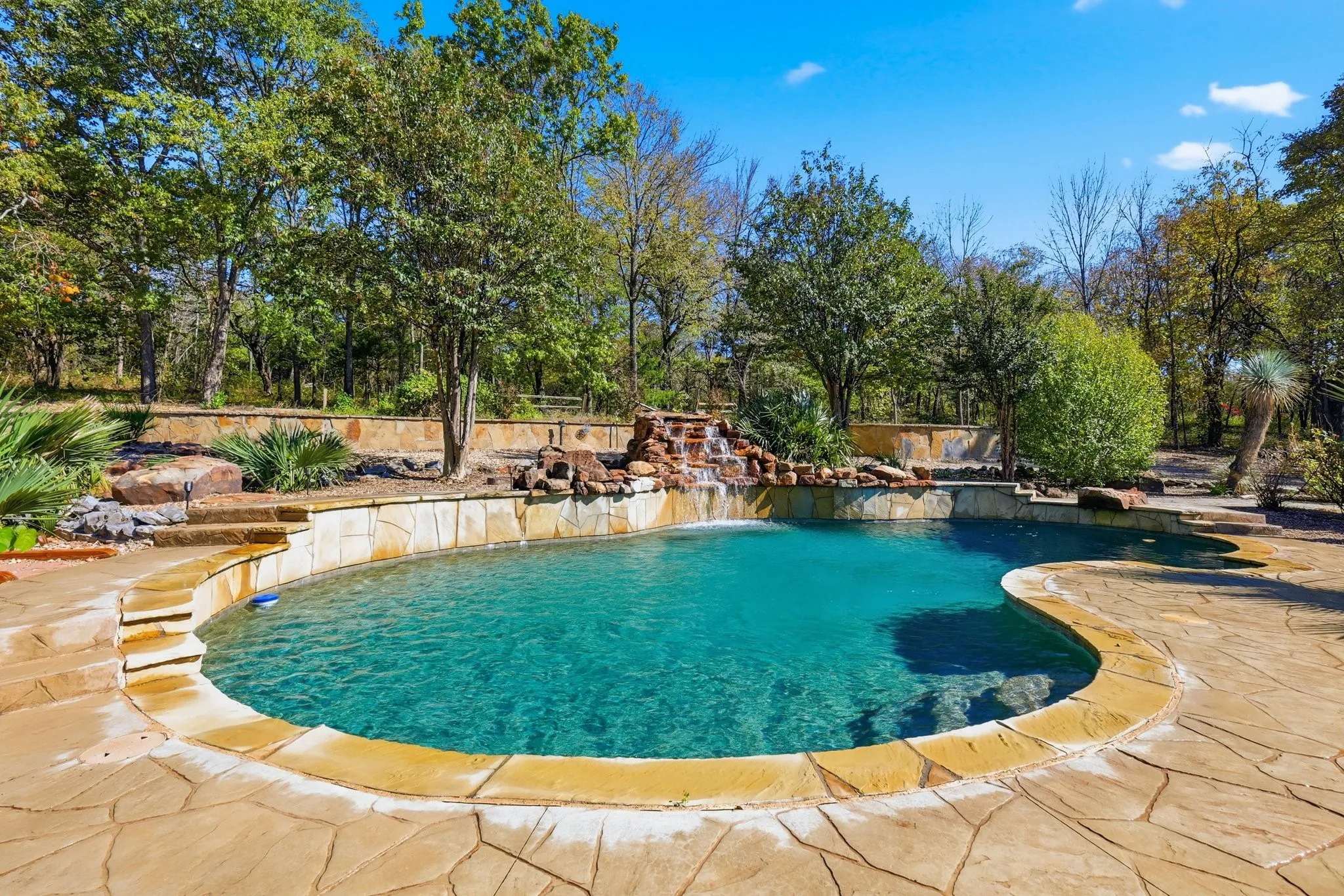 Rock Waterfall Spilling into a Resort Style Diving Pool Surrounded By Mature Trees and Natural Stone Decking. Your Own Private Margaritaville! Stamped Cement Decking and Flagstone Decking.