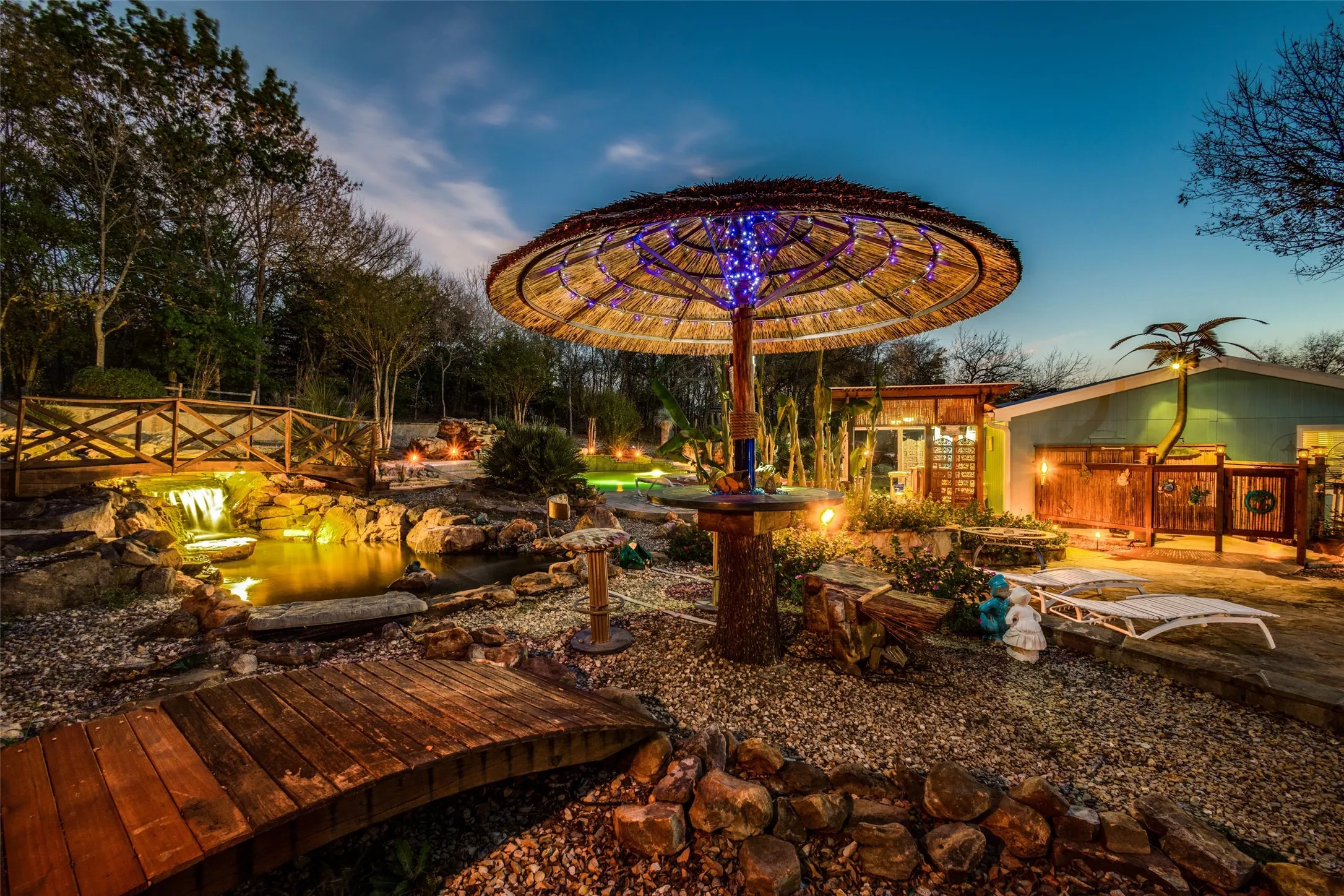 Twilight Transforms This One of a Kind Retreat with Glowing African Thatched Umbrellas, Custom Bridges, and a Lighted Koi Pond with Waterfall and Japanese Koi. Plenty of Room For Large Gatherings, Celebrations, and Unforgettable Nights Under the Warm Island Inspired Lights.