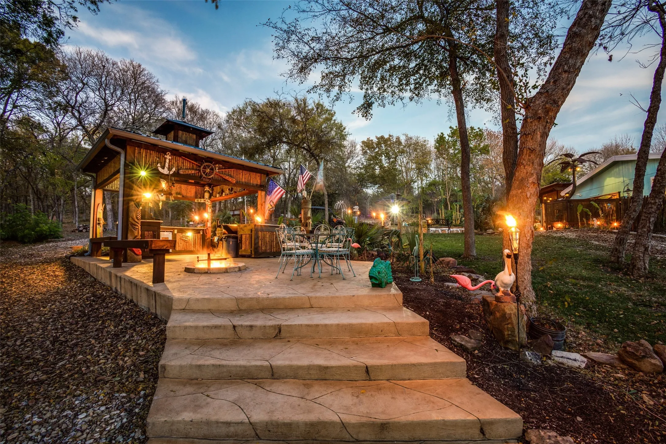 Your Private Margaritaville! Tropical Island Tiki Hut, Torches, Party Lights, and Warm Twilight Glow Set the Stage For a One of a Kind Backyard Escape.