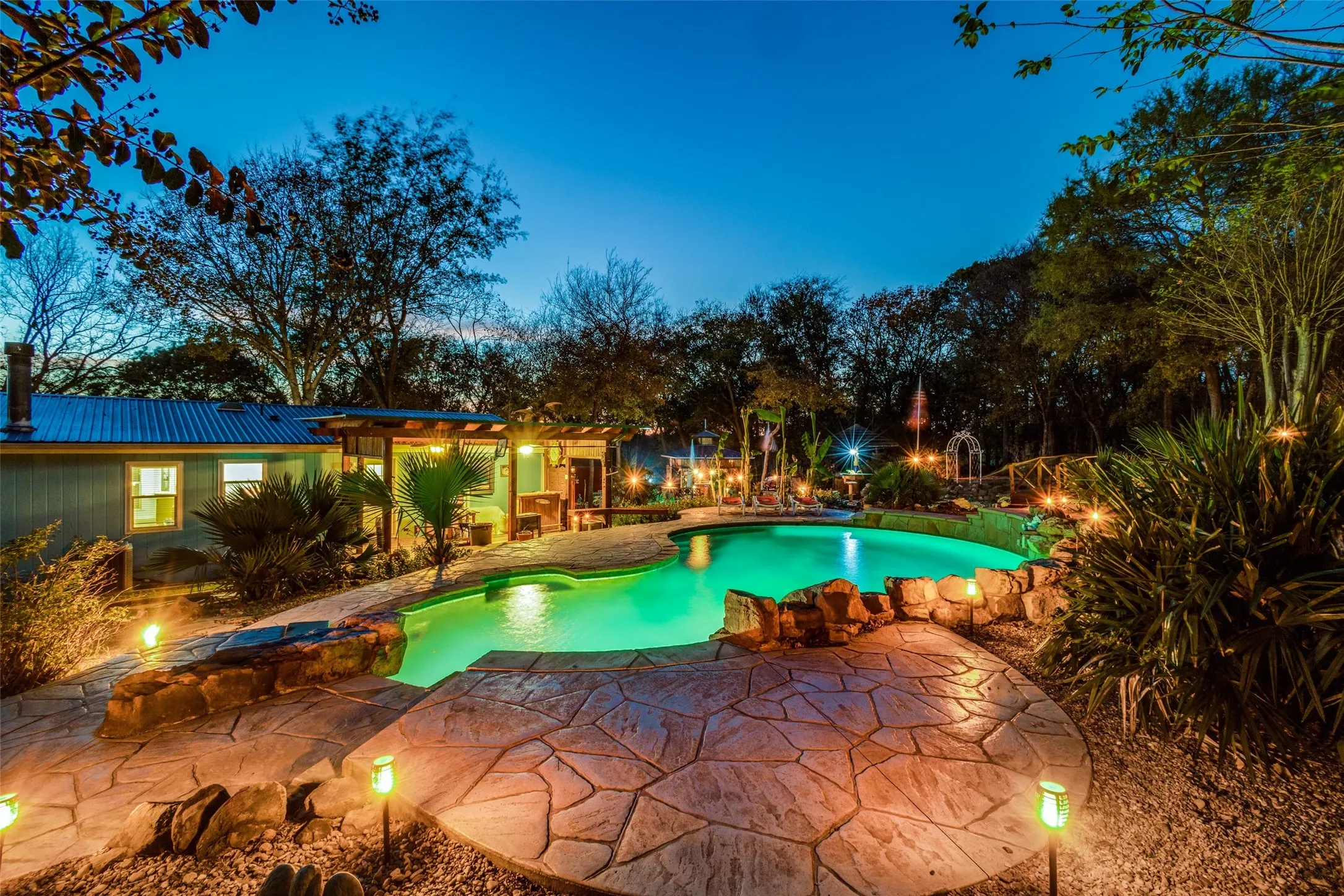 Tranquil Resort Style Pool with Waterfall, Tanning Ledges, Pergola, Landscape Lighting, Offering a Peaceful Escape with Sweeping Views of the Beautiful Countryside.