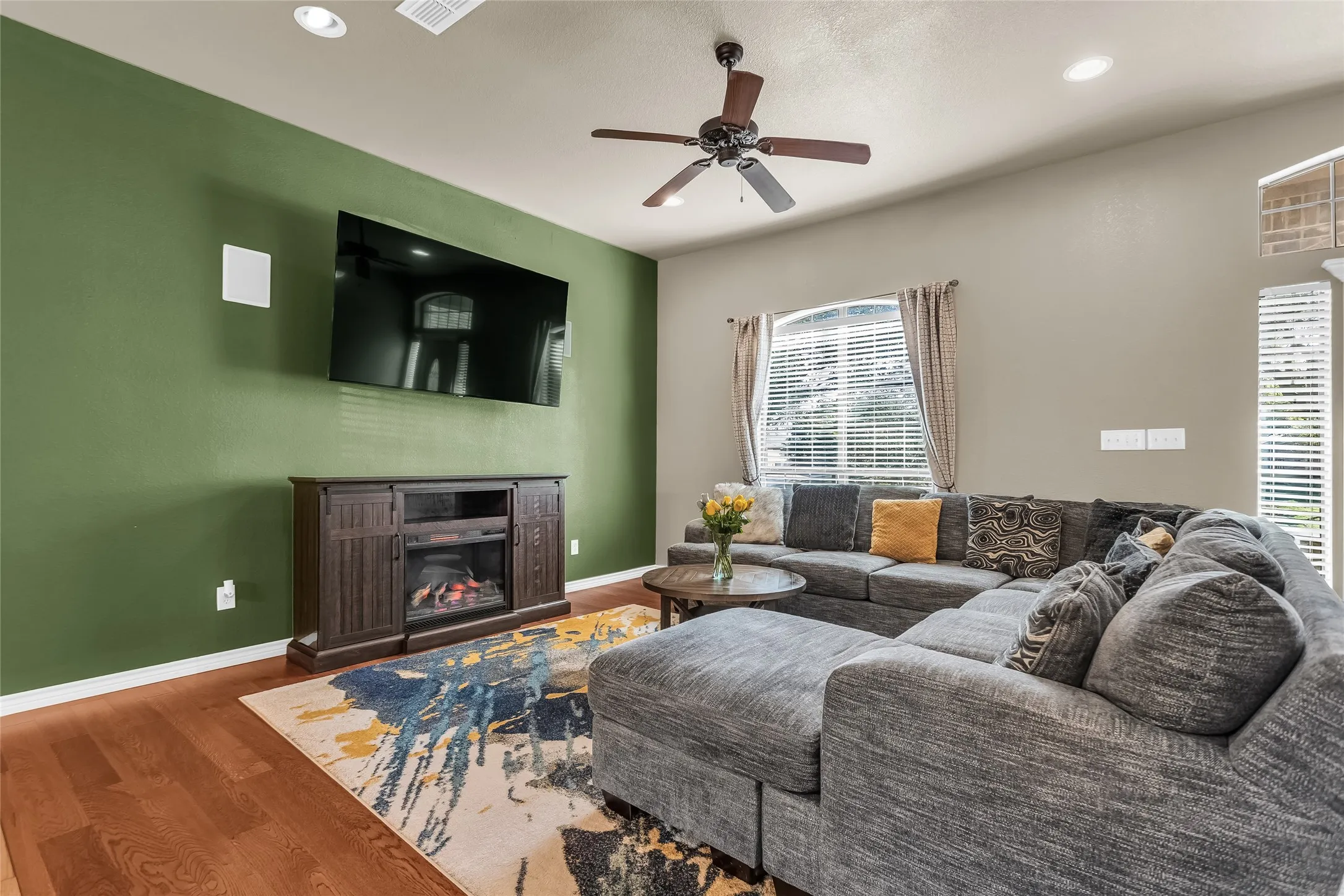Living room featuring wood finished floors, a glass covered fireplace, a ceiling fan, and recessed lighting