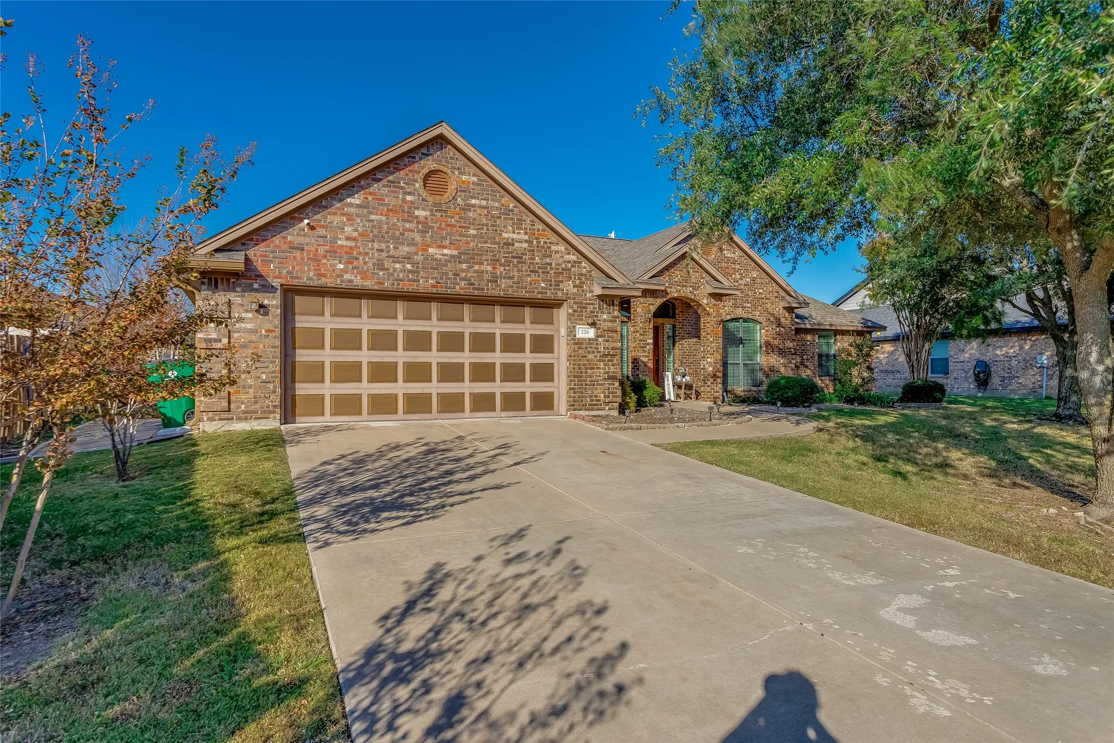 View of front facade featuring a front lawn, concrete driveway, brick siding, and an attached garage