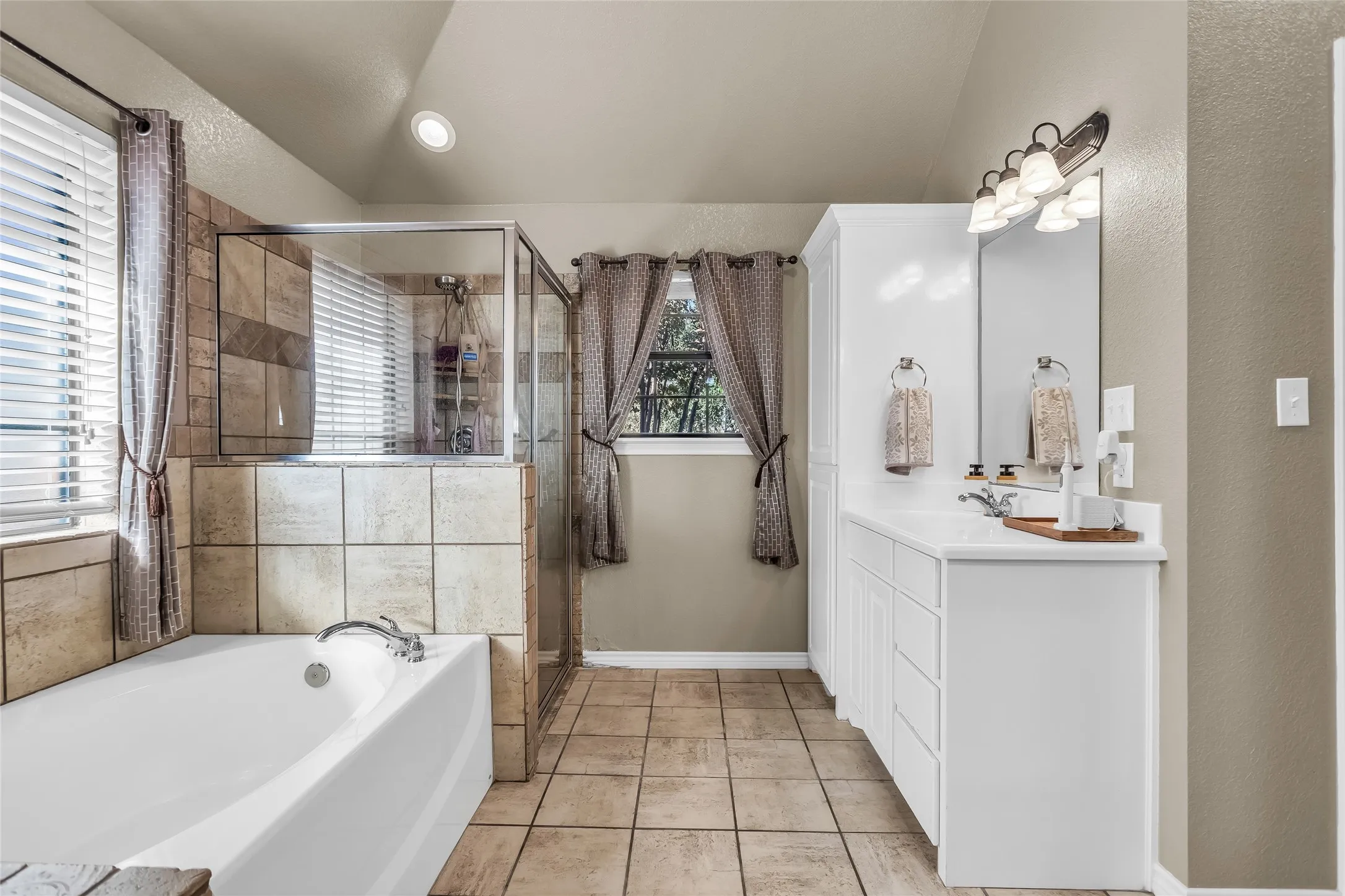 Bathroom featuring vanity, a textured wall, light tile patterned floors, a bath, and a shower stall